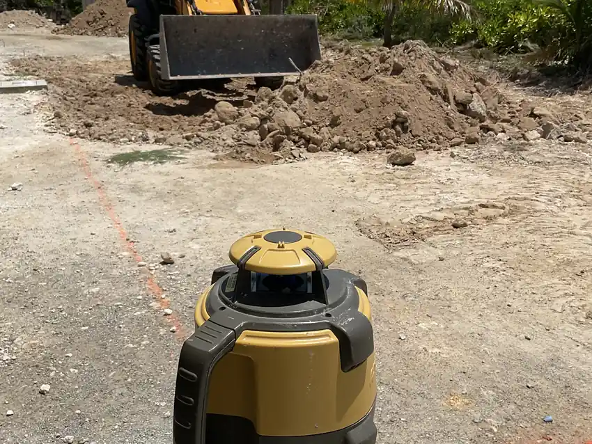 Rotating laser level set up on cleared ground with an excavator working behind it