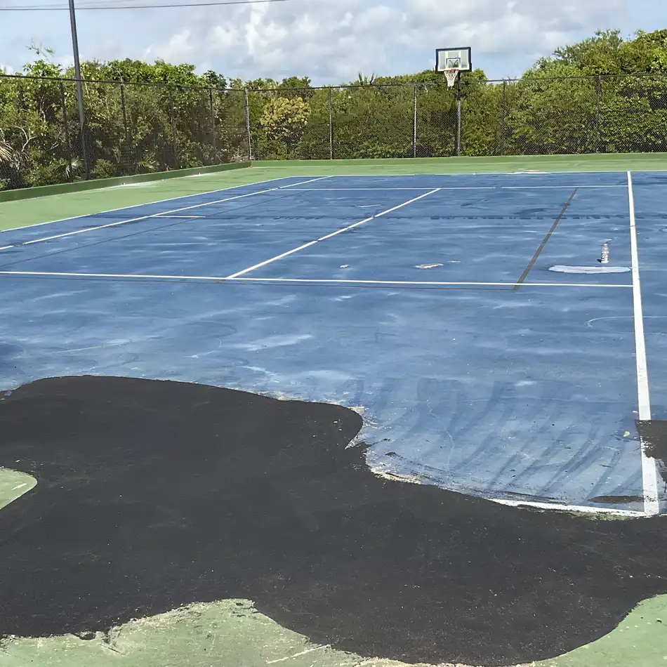 Large asphalt patch laid across the corner of a playing surface, meeting the older coating